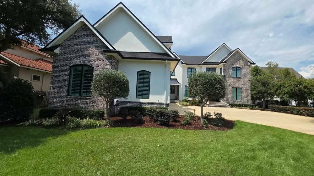 Modern two-story house with brick and white siding, manicured lawn, landscaping, and driveway on a sunny day