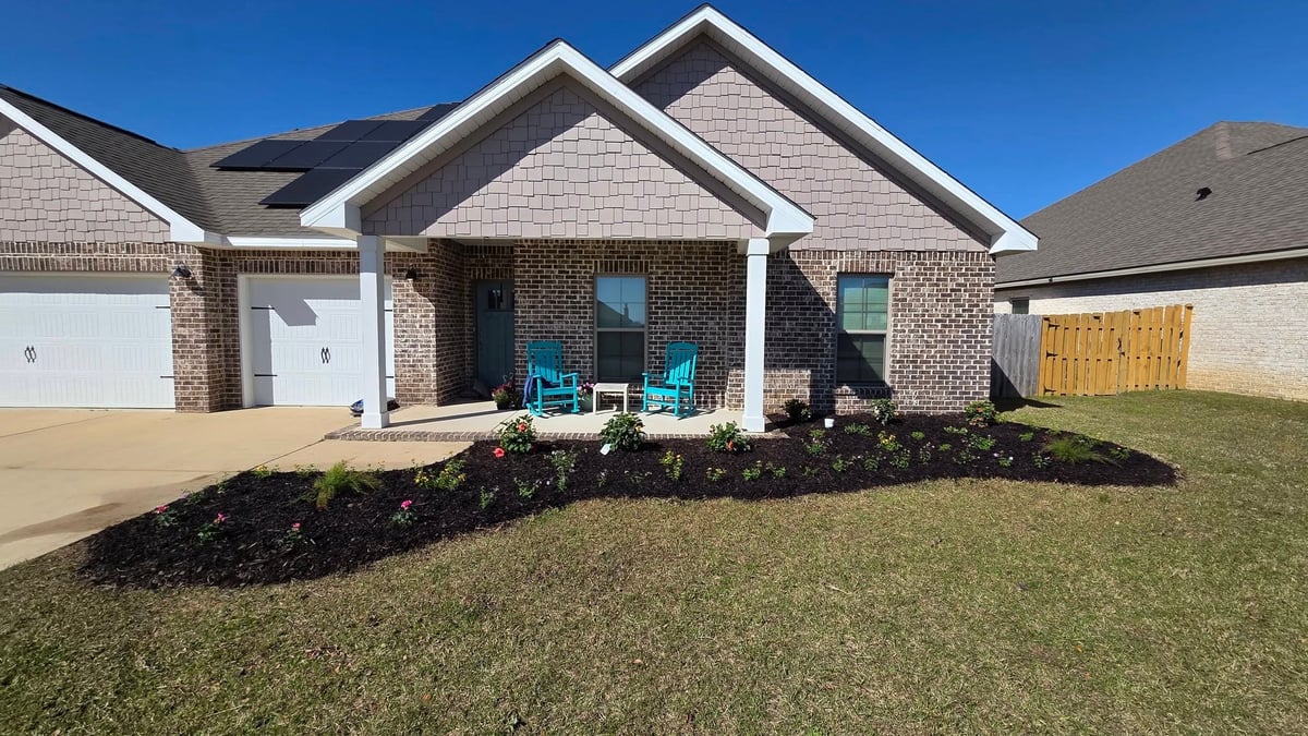 Single-story brick home with white trim, garage, blue front porch seating, and mulch landscaping on a clear day