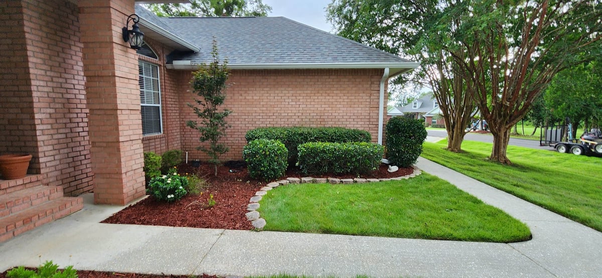 Brick house with red mulch landscaping, green shrubs, manicured lawn, and driveway entrance