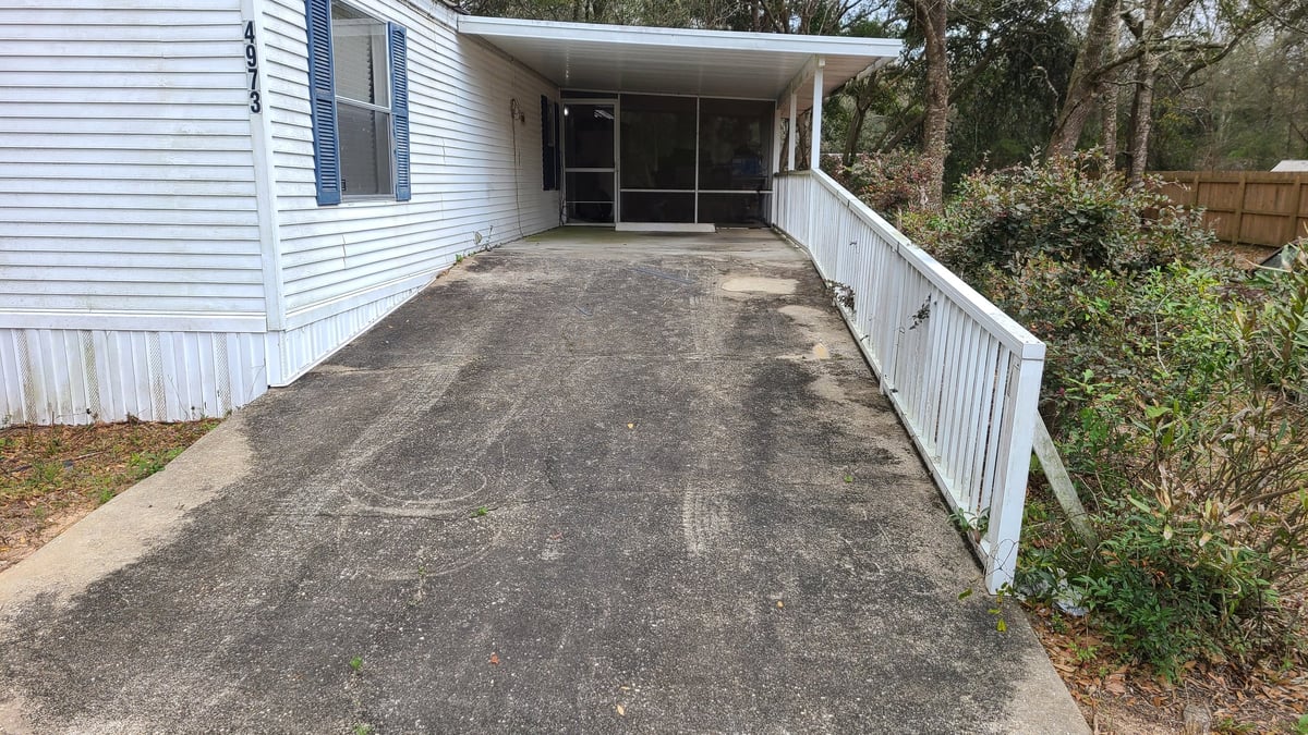 Asphalt driveway leading to a mobile home with white siding and metal railings on both sides