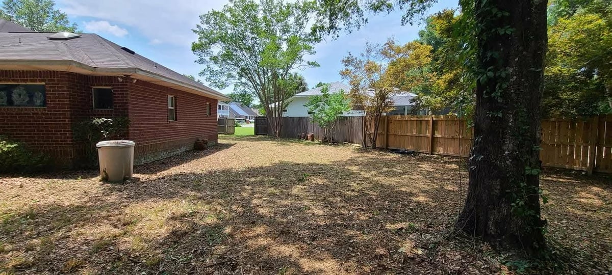 Spacious backyard with brick house, large shade tree, wooden fence, and landscaped lawn