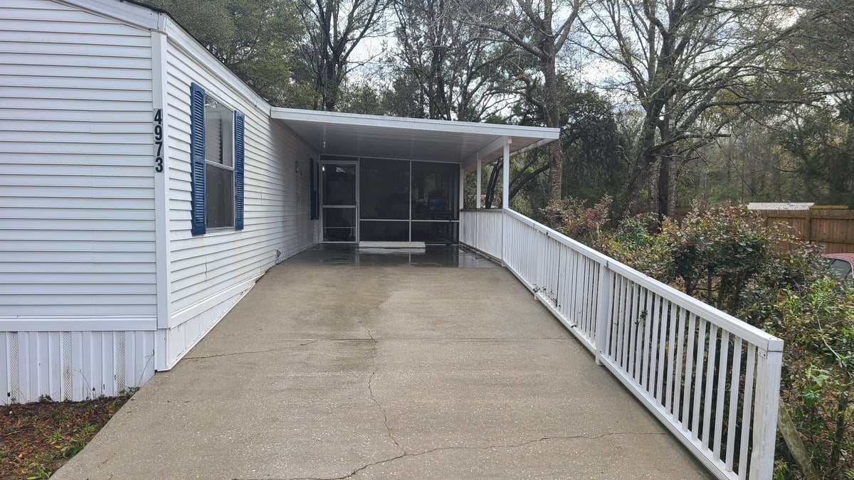 White mobile home with concrete patio and white railings surrounded by bare trees