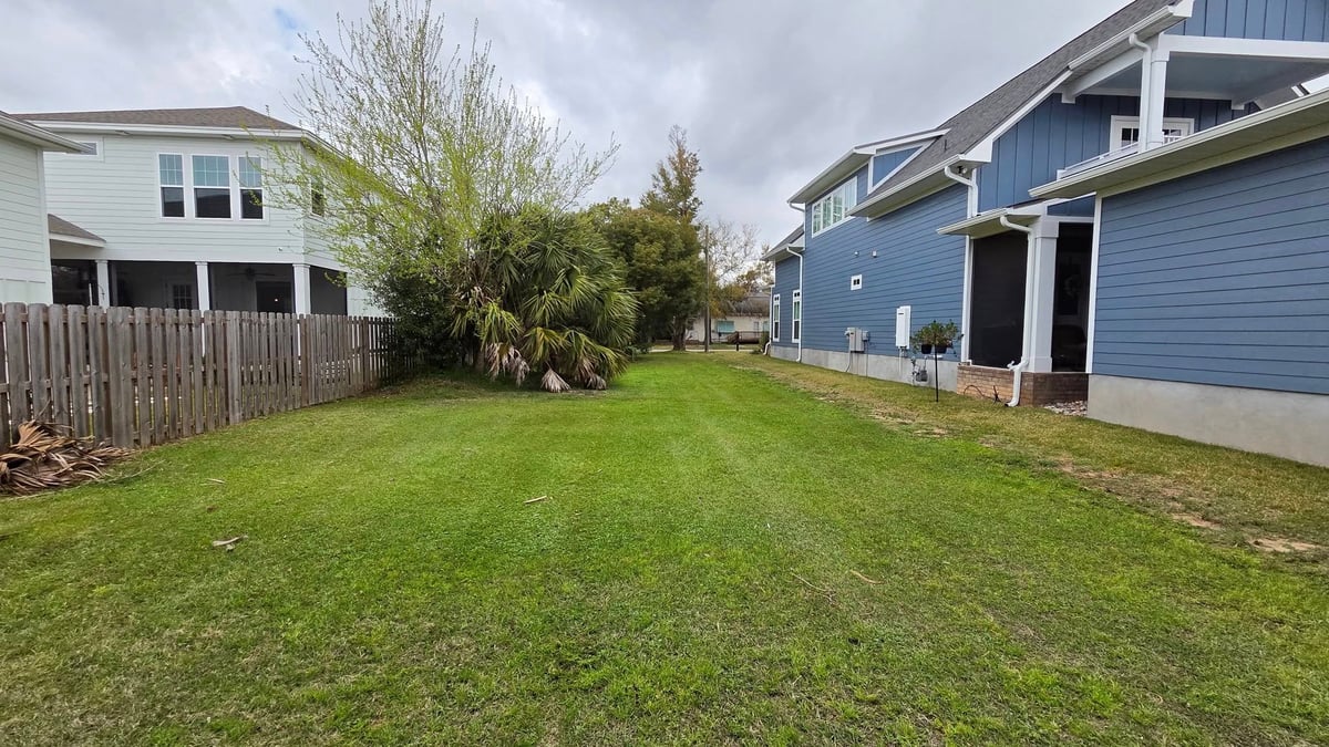 Spacious green lawn between residential houses with blue and white siding on a cloudy day
